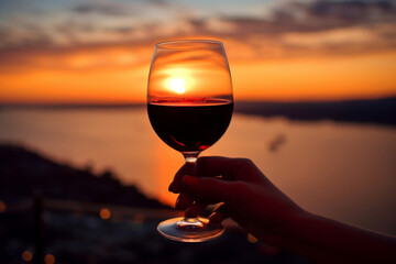 Fototapeta na wymiar A glass of red wine, in hand, against the backdrop of sunset. AI generation