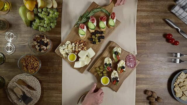 Beautiful serving of delicious appetizers and bruschettas on a wooden board. An unrecognizable woman puts a board with snacks on the table.