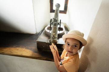 Little girl in a hat and a yellow T-shirt with a vintage cannon in castle.