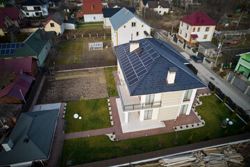Aerial drone view of house with photovoltaic solar panels on rooftop surrounded by yard, road and...