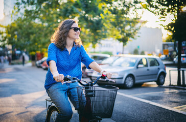 Caucasian young curly woman in sunglasses riding a bicycle on a city street at summer sunset.