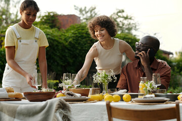 Happy young woman embracing her husband and serving table with their daughter while preparing for family dinner in natural environment