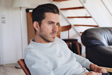 A man looks sad and thoughtful, sitting on a couch at home