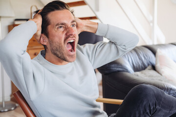 Young handsome man screaming angry and emotionalon a couch at home