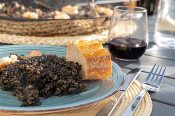 Black rice with squid and shrimps in a paella pan. Ready to eat, with bread and red wine