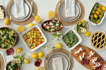 Top view of served dinner table with napkins on plates, fresh lemons, homemade vegetables, salads, sandwiches, juice, lemonade and sweet pie