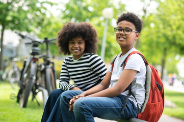 Two friends young girl boy sitting on bench in park enjoying summer green outdoors. © zinkevych