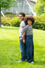 Boy and girl having fun in park standing back to back playing outdoor during summer vacation.