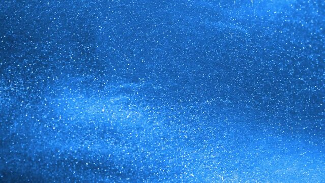 Chaotic layered motion of silvery dust particles in a blue fluid. Light glittering particles float in a blue liquid. Abstract moving background 4K resolution.