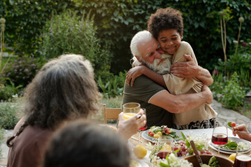 Affectionate senior man embracing his African American grandson while sitting by dinner table...