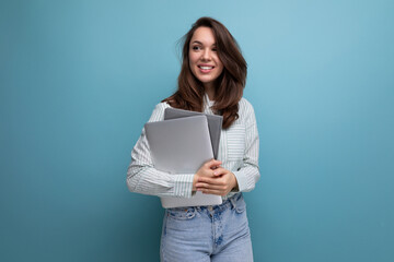 IT specialist 25 year old brunette woman in shirt and jeans enjoys freelancing holding a laptop in...