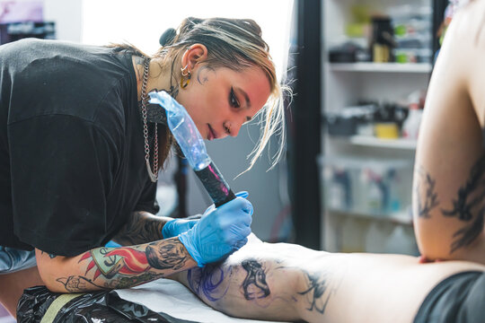 Tattooing process. Indoor portrait of focused female tattoo artist drawing on leg of her favourite female client. . High quality photo
