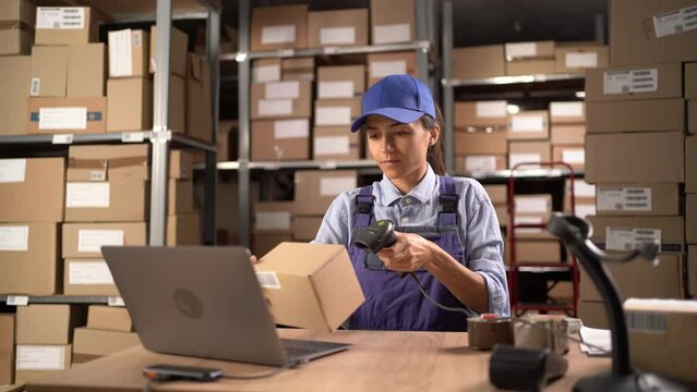 Warehouse woman worker with barcode scanner sitting at the table with laptop computer