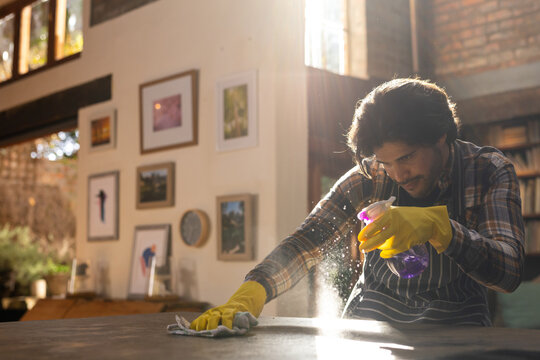 Indian Man Wearing Yellow Gloves And Cleaning Worktop In Kitchen, Copy Space