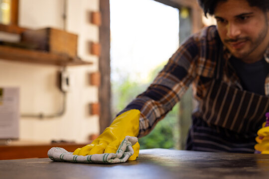 Indian man wearing yellow gloves and cleaning worktop in kitchen, copy space