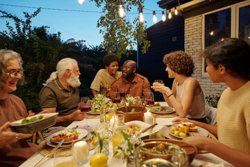 Cute boy and his father sitting by served table among other members of family while enjoying...