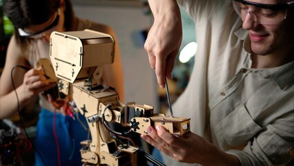 Two young engineers fixing a mechanical robot in the workshop, wearing industrial glasses