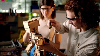 Two young engineers fixing a mechanical robot in the workshop, wearing industrial glasses
