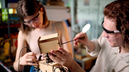 Two young engineers fixing a mechanical robot in the workshop, wearing industrial glasses
