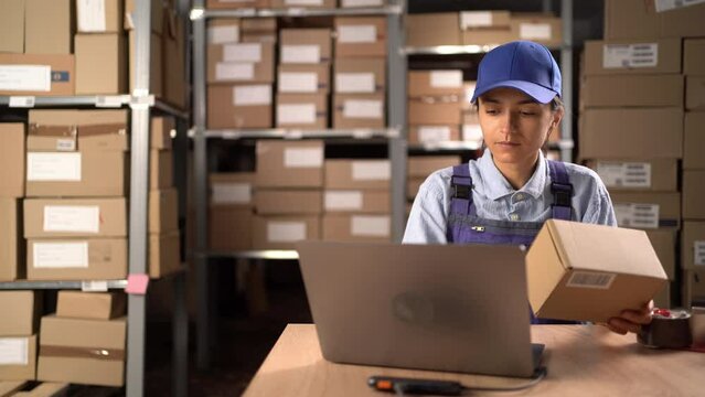 Female manager checks stock and inventory on laptop computer in the retail warehouse full of shelves with goods. People Working in logistics, distribution center
