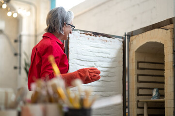 Positive craftswoman standing in front of open pottery kiln working in pottery workshop.