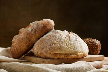 Assortment of baked bread on wooden table over brown studio background.