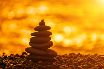 Balanced rock pyramid on pebbles beach. Golden sea bokeh on background. Selective focus, zen stones on sea beach, meditation, spa, harmony, calm, balance concept.