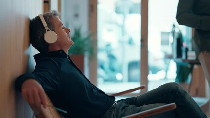 Video of mature handsome entrepreneur man relaxing while listening to music with headphones in a coworking place - Powered by Adobe