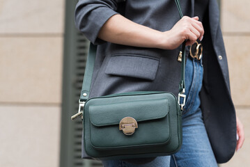 A woman holds a green handbag in the city. Close-up image. The concept of luxury - obrazy, fototapety, plakaty