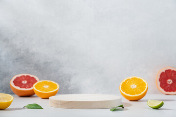 Empty wooden round podium on light grey background surrounded by citrus fruits. Display, pedestal for the presentation of cosmetic products, drinks