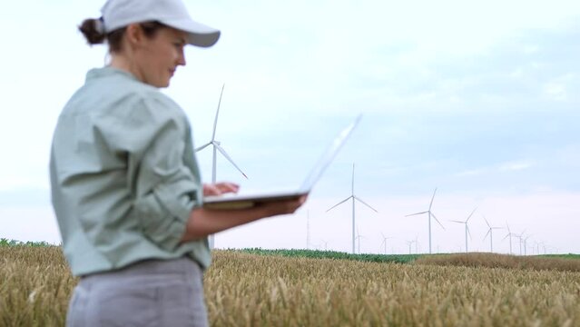 Farmer with laptop on a wheat field, wind turbines on the horizon