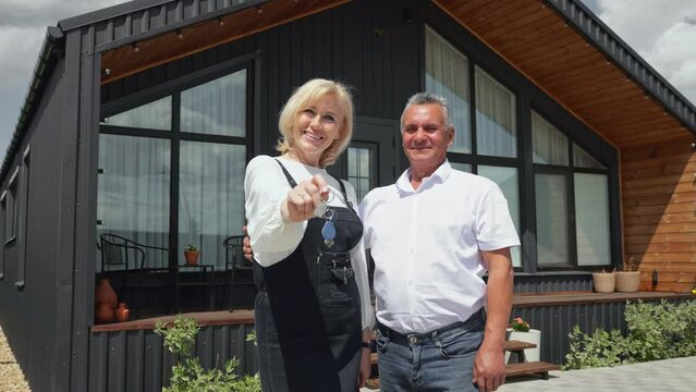 Happy husband and blonde wife with keys to new vacation house in country. Family owners of cottage residence provided by real estate company