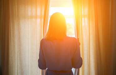 Fototapeta premium Woman opening curtains in the room at sunny morning.