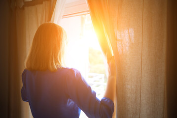 Obraz premium Woman opening curtains in the room at sunny morning.