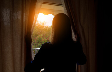 Fototapeta premium Woman opening curtains in the room at sunny morning.