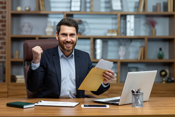 Obraz premium Portrait of happy businessman investor, mature adult man smiling and looking at camera, boss holding message envelope with good winning news inside office at workplace.