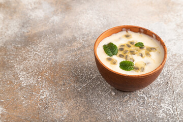 Yoghurt with granadilla and mint in clay bowl on brown concrete, side view, copy space.