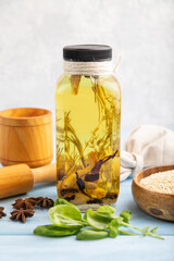 Sunflower oil in a glass jar with various herbs and spices on a brown concrete. Side view, selective focus.