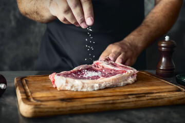 Man cook sprinkles salt on a fresh raw beef steak on the bone