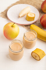 Baby puree with fruits mix, apple, banana infant formula in glass jar on white, side view