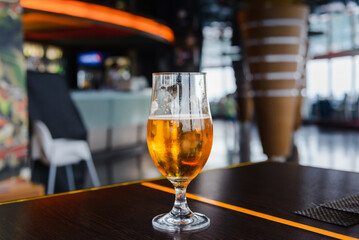 A beer in Tulip glass. Glass of light beer on wooden table in cafe or restaurant .Beautiful crystal glass with golden freshly brewed cold wheat beer stands on table cafe,restaurant terrace.