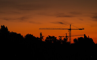 Cranes silhouette in morning dusk sunrise light. Sunrise photo with cranes and the reflection on a lake. Construction industry.