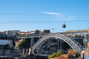 Imagen de uno de los famosos puentes de la ciudad portuguesa de Oporto con el teleférico cruzando el río Duero por las alturas. - obrazy, fototapety, plakaty