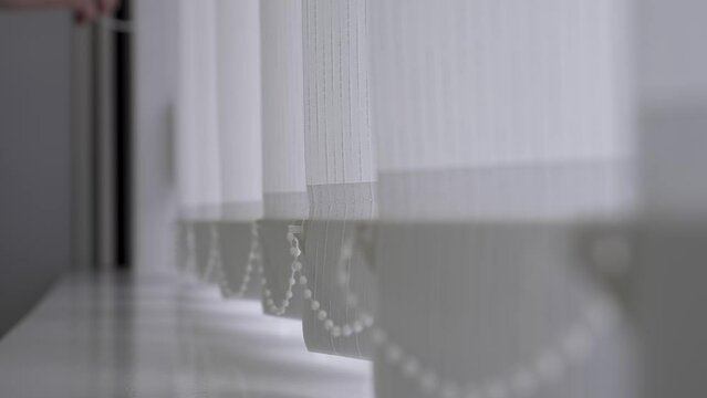 the concept of home comfort
close-up of a window in a home or office with white blinds
vertical light blinds are opened or retracted to create exactly the kind of lighting in the room as needed