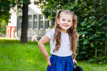 Adorable little schoolgirl is standing outdoors on bright autumn day.