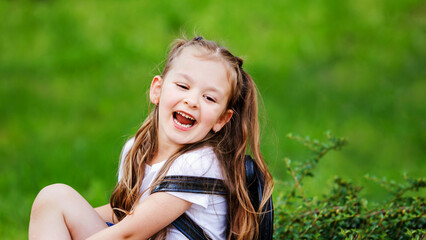 Adorable little girl is sitting on the grass and laughing.