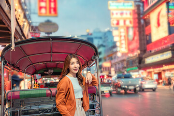Happy young tourist Asian woman enjoy three wheel open air taxi and fun traditional asian street food at night Bangkok Chinatown, Female shopping street food on summer holiday vacation.