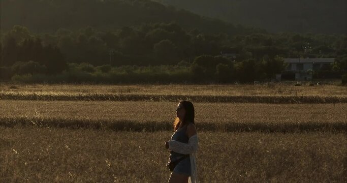 Chica andando por atardecer por el campo de trigo