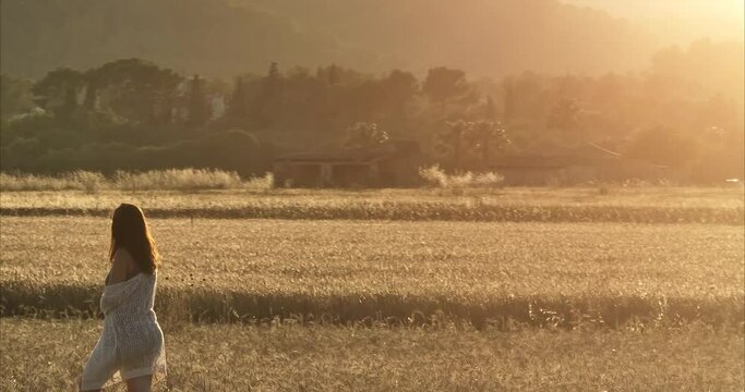 Chica andando por atardecer por el campo de trigo