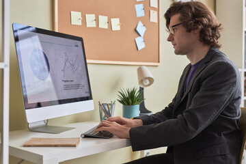 Side view portrait of smiling long haired man using computer at desk in office or at home workplace